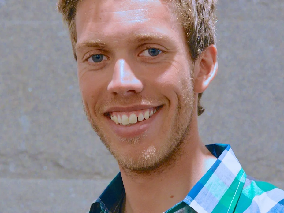 Marcus Hellner ler mot kameran i rutig skjorta framför en grå stenvägg 2013