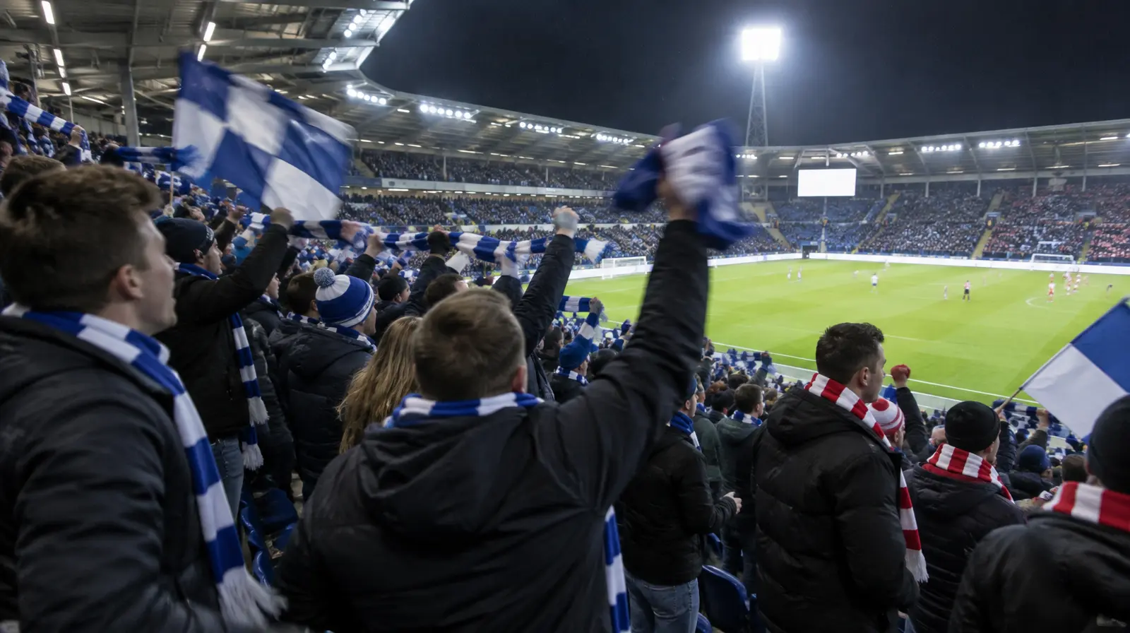Supportrar reagerar på läktaren i kvällsljus, med halsdukar och flaggor i lagfärgerna