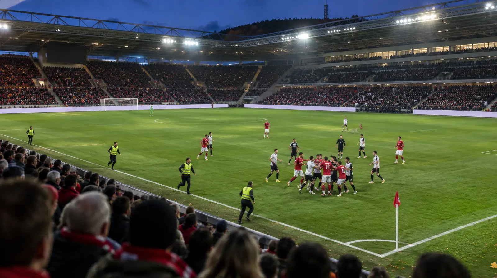 Spelare samlas vid sidlinjen i kvällsljus på en tysk fotbollsarena